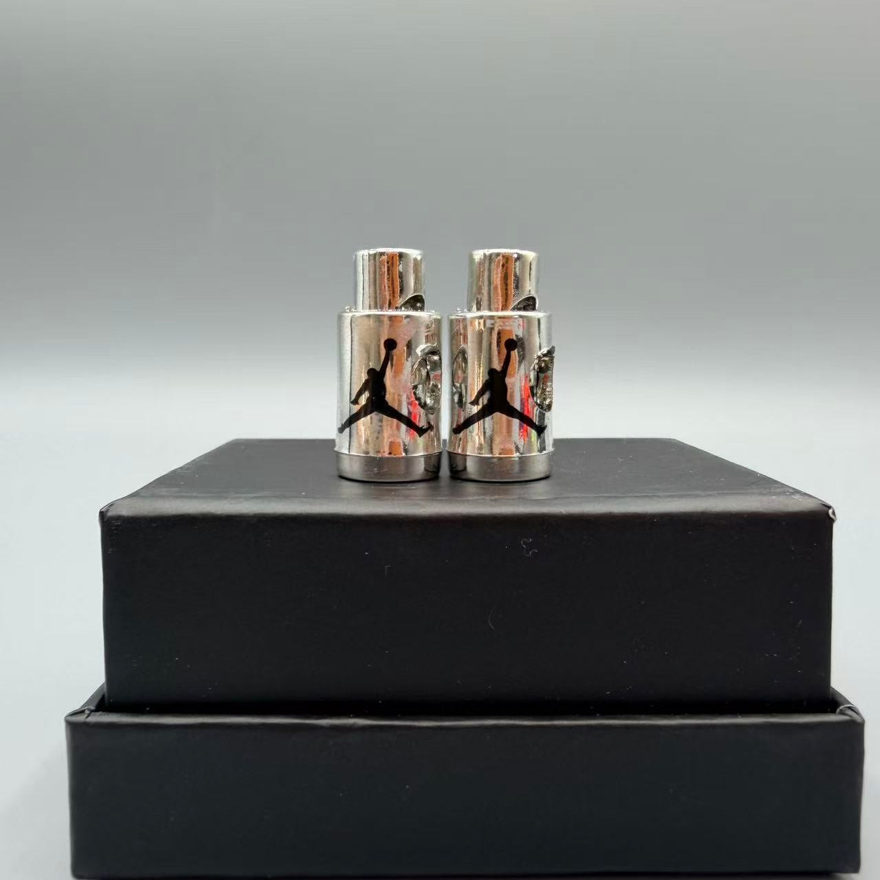 Silver cufflinks with a logo on a black box against a gray background