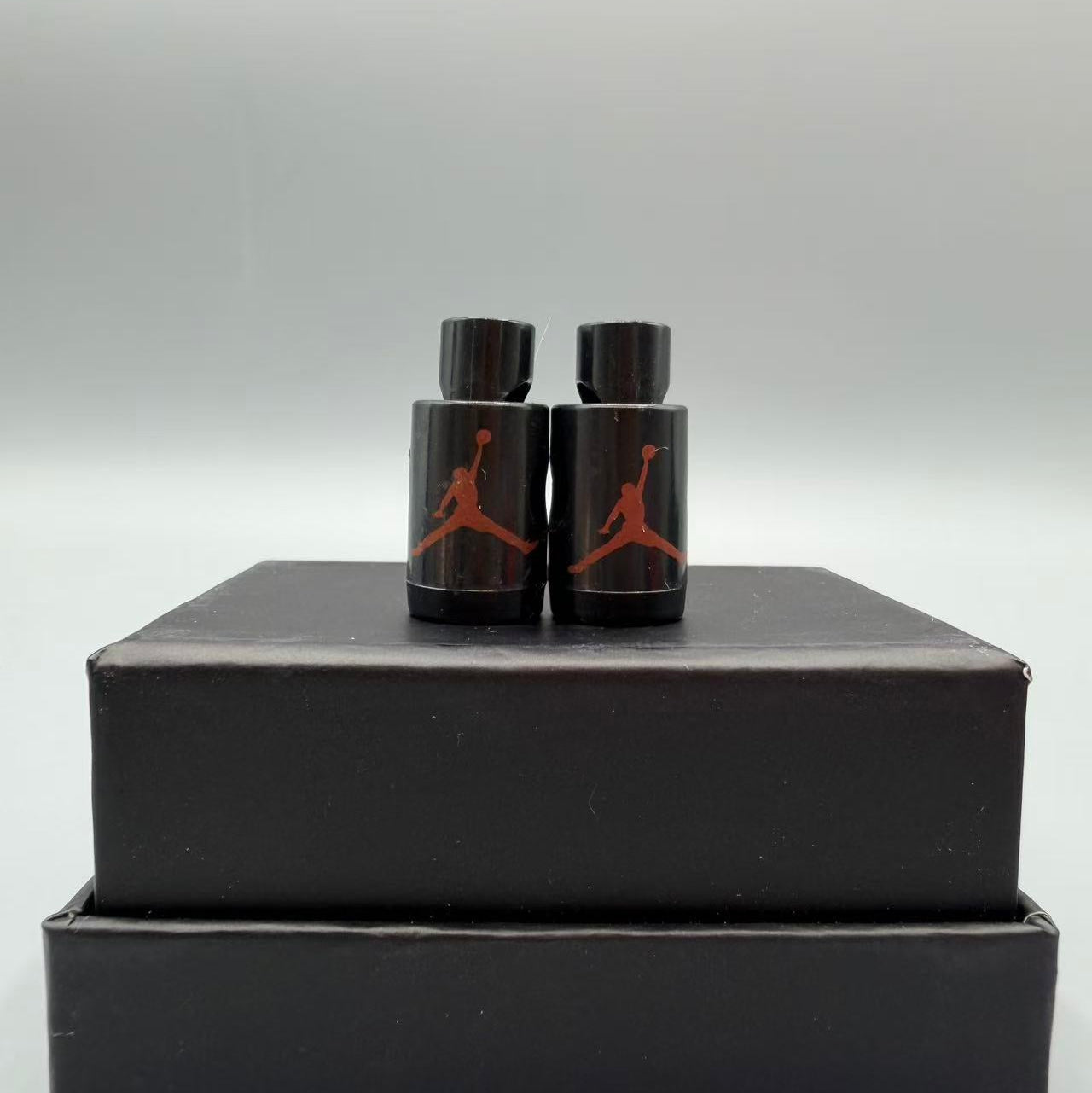 Two black jordan lace locks with a red logo on top of a black rectangular box against a gray background.